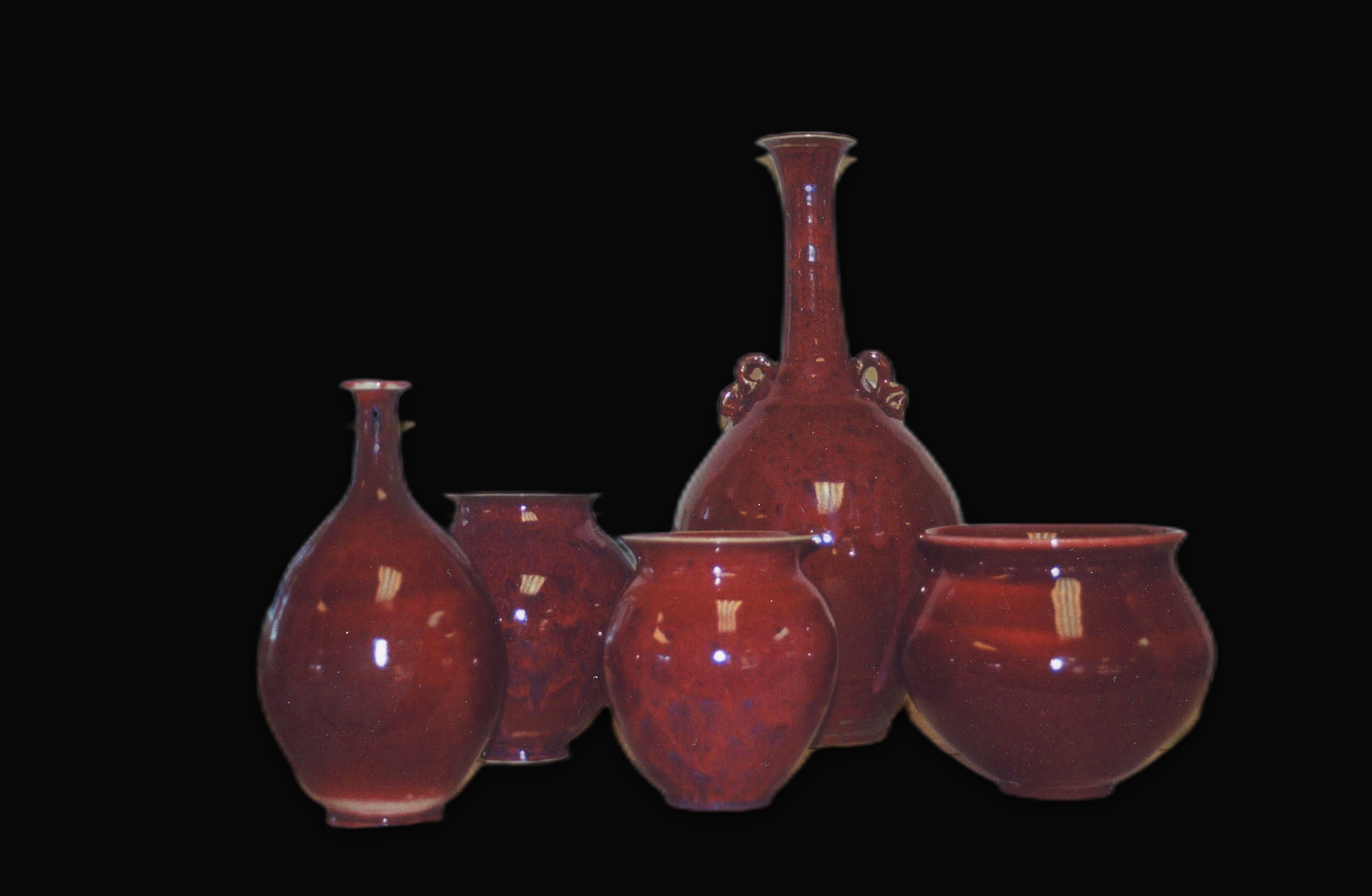 Group of oxblood red glazed ceramic vessels on a black background